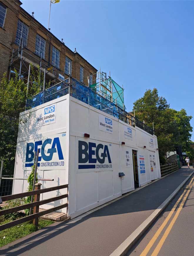 Construction site hoarding with BEGA and NHS West London logos.