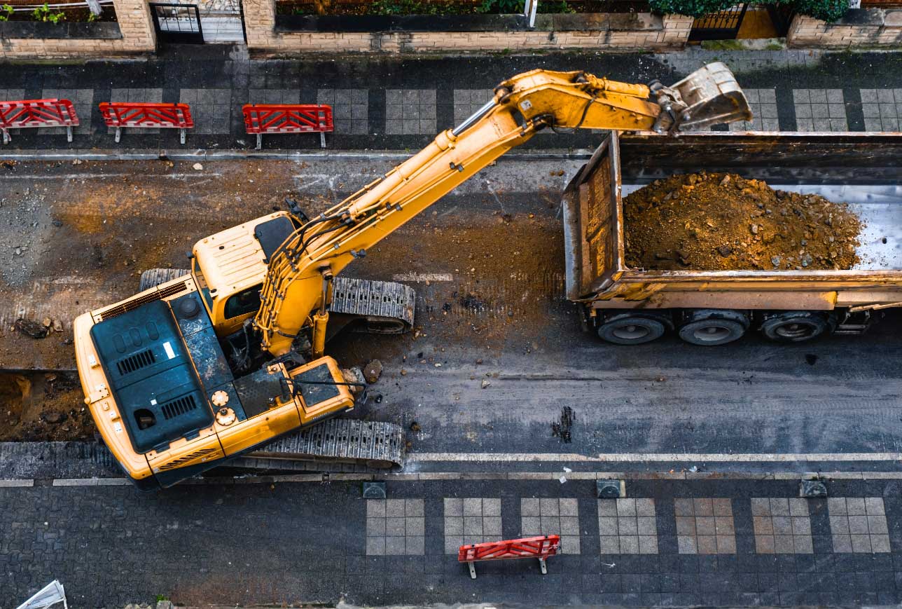Excavator loading earth into a truck during street excavation.